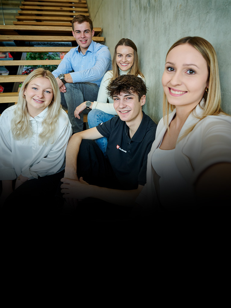 Fünf junge Erwachsene sitzen auf einer Treppe und machen ein Selfie, der Hintergrund ist teils dunkel.
