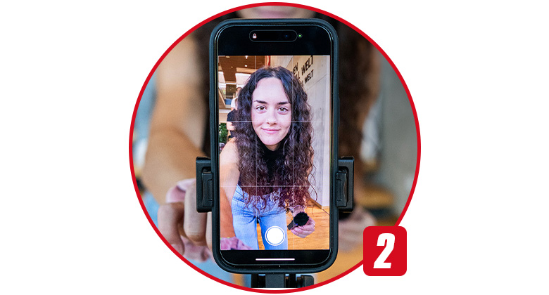 Eine Frau mit lockigem Haar macht ein Selfie mit einem Smartphone, das in einer Halterung befestigt ist.