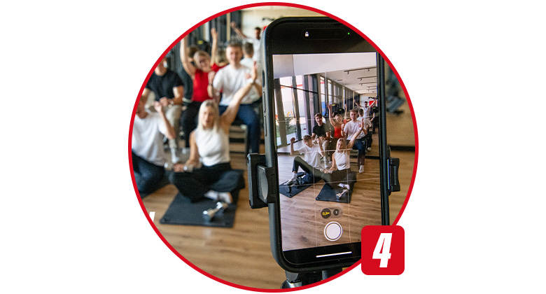 Eine Gruppe posiert auf Sportmatten, aufgenommen durch ein Smartphone auf einem Stativ.
