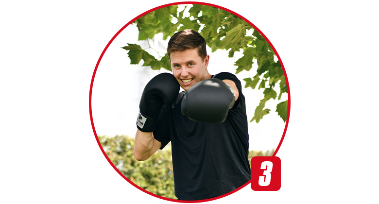 Ein junger Mann mit schwarzen Boxhandschuhen steht in Kampfhaltung im Freien.