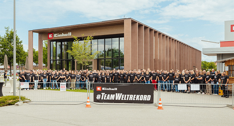 Eine große Gruppe von Einhell-Mitarbeitern in schwarzen T-Shirts posiert hinter einem Banner mit der Aufschrift „#TeamWeltrekord“.
